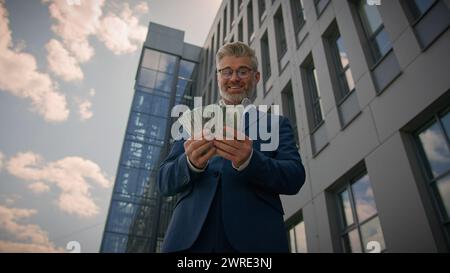 Felice e gioioso successo ricco vecchio ricco uomo caucasico anziano imprenditore maturo imprenditore d'affari in centro città buttare soldi pioggia in aria Foto Stock