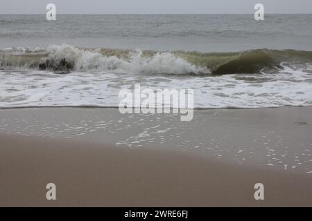 Onde con creste bianche inondare la spiaggia sabbiosa Foto Stock