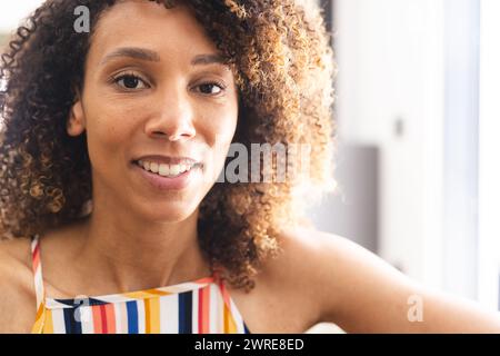 Donna birazziale con capelli ricci sorride calorosamente, indossando un colorato top a righe Foto Stock