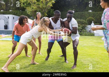 Gruppo di amici diversi che giocano a calcio in un cortile soleggiato, risate evidenti Foto Stock