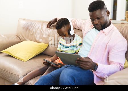 Padre e figlio afroamericani si godono un tablet insieme su un divano Foto Stock