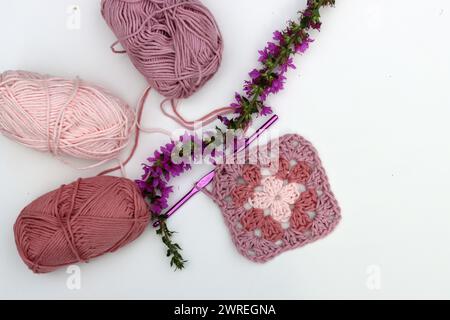 Quadrato di nonna all'uncinetto rosa, palle di filato di cotone morbido di diverse tonalità di colore rosa. Sfondo bianco con spazio di copia. Concetto di uncinetto primaverile. Foto Stock