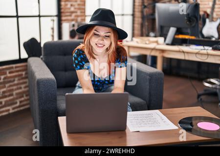 Giovane musicista caucasica sorridente sicuro di usare il portatile in studio musicale Foto Stock