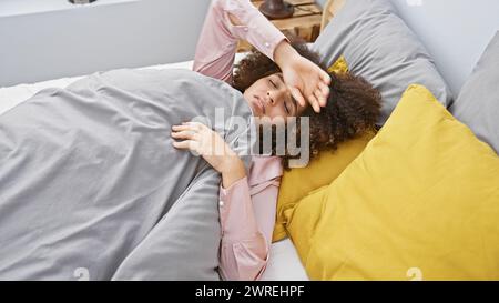 Una giovane donna ispanica con i capelli ricci sdraiata a letto a casa, che sembra stanca o malata. Foto Stock