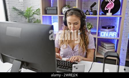 Elegante e giovane donna ispanica, che indossa le cuffie, completamente immersa nel suo videogioco ad alta quota, dal comfort della sua elegante stanza da gioco, Foto Stock