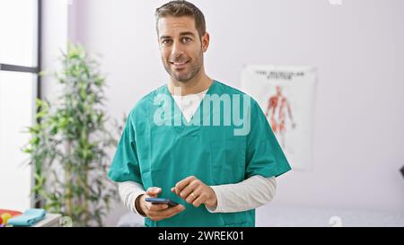Uomo ispanico in scrub con smartphone in piedi al chiuso alla clinica Foto Stock
