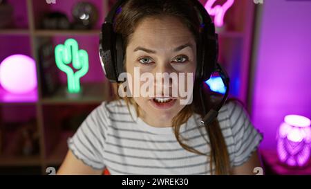 Una donna concentrata con le cuffie in una sala giochi colorata guarda con attenzione lo schermo. Foto Stock