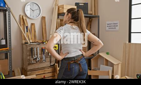 Vista posteriore di una giovane donna in piedi con sicurezza in un'officina di falegnameria ben attrezzata. Foto Stock