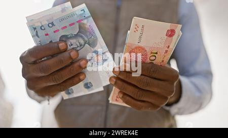 Uomo africano in abbigliamento formale che tiene in mano yuan cinese e valuta estera in una strada urbana. Foto Stock