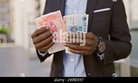 Uomo africano in tuta con yuan cinese e altre valute in città Foto Stock