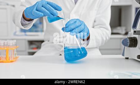 Uno scienziato maschio in un laboratorio che versa liquido blu da un becher in una fiasca. Foto Stock