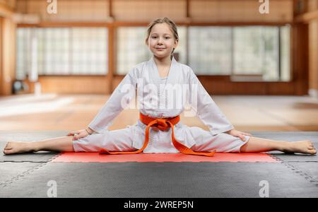 Allegro bambino in uniforme di karate esegue una spaccatura su un tappetino Foto Stock