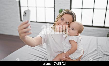 Madre e figlia felici che scattano selfie sicuri e catturano momenti preziosi di amore e di amicizia nella comoda stanza seduti sul letto, facendo foto Foto Stock