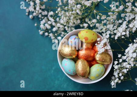 Le uova di cioccolato pasquale avvolte con un foglio di carta in un recipiente di vetro. Concetto di festa di Pasqua. Natura morta colorata con dolci. Sfondo testurizzato con spazio di copia. Foto Stock