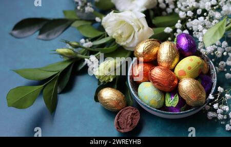 Le uova di cioccolato pasquale avvolte con un foglio di carta in un recipiente di vetro. Concetto di festa di Pasqua. Natura morta colorata con dolci. Sfondo testurizzato con spazio di copia. Foto Stock