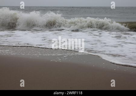 Onde con creste bianche inondare la spiaggia sabbiosa Foto Stock