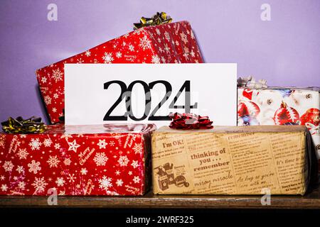 Lavagna con l'iscrizione 2024 isolata su sfondo viola e regali colorati in giro, le festività stanno arrivando, Natale è vicino. Foto Stock