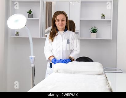 Donna cosmetologa in piedi e che guarda la macchina fotografica nel salone di bellezza del centro benessere. Dermatologa femminile, terapista della pelle, estetista e SkinCare professionista in clea Foto Stock