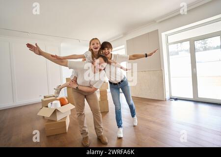 Genitori gioiosi che giocano in aereo con il loro bambino in una nuova casa Foto Stock