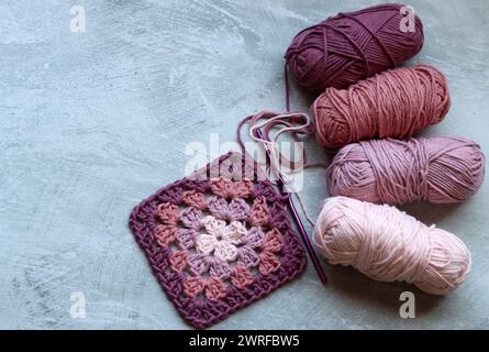 Motivo a uncinetto quadrato nonna. Foto colorata di filati organici rosa tenue. Concetto di hobby e svago. Sfondo grigio chiaro con spazio di copia. Foto Stock