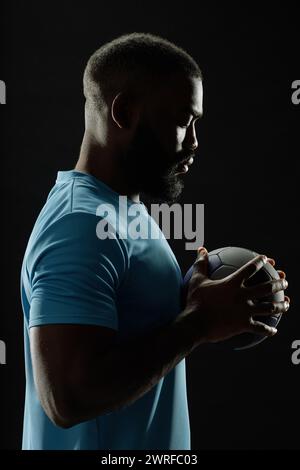 Spettacolare ritratto laterale del giocatore di football afroamericano che tiene la palla su sfondo nero con contorno Foto Stock