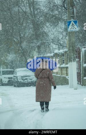 L'immagine di una stagione invernale che nevica molto duramente e ci sono fiocchi mascherati. Nonna con un ombrello mentre c'è un ciclone fuori. Una vittoria forte Foto Stock