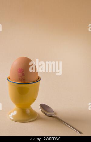 Un uovo bollito in una tazza con cucchiaio Foto Stock