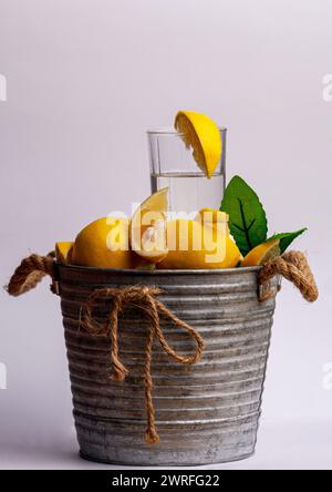 Immagine su sfondo bianco con un calderone pieno di frutta chiamata lime. Al centro del frutto c'è un bicchiere pieno d'acqua con una fetta Foto Stock