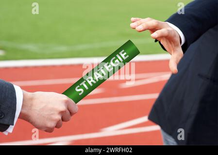 Gli uomini d'affari passano il testimone con la parola tedesca strategia in gara affidata allo stadio Foto Stock