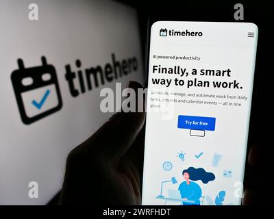 Persona che detiene lo smartphone con la pagina web della società canadese TimeHero Inc. Davanti al logo aziendale. Messa a fuoco al centro del display del telefono. Foto Stock