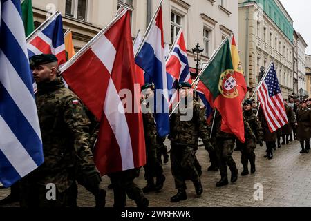 I soldati polacchi marciano le bandiere dei membri della NATO mentre la Polonia celebra il 25. Anniversario dell'adesione all'alleanza del Nord Atlantico nella piazza principale nella città vecchia di Cracovia, in Polonia, il 12 marzo. 2024. Foto Stock