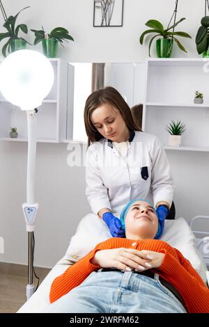 Il cosmetologo estetista prepara il cliente per la procedura o i trattamenti facciali in un salone. Cosmetologia hardware nel salone clinico per l Foto Stock