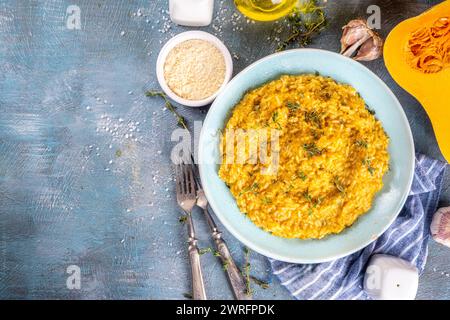 Delizioso risotto di zucca al formaggio fatto in casa con parmigiano e timo, con ingredienti e spezie su una tavola di cemento blu Foto Stock