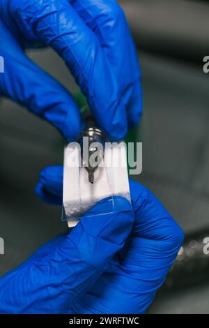Le mani con guanti fotografici verticali posizionano meticolosamente un nuovo ago per tatuaggio, garantendo la sterilizzazione e la precisione del processo di tatuaggio. Concept business, Foto Stock