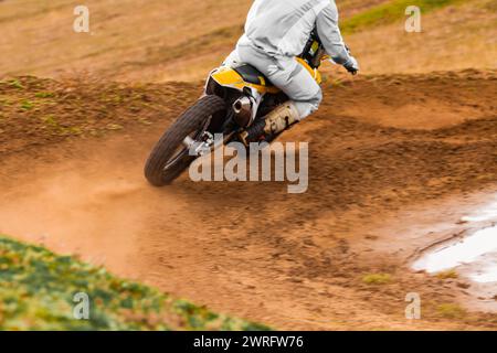 La persona sta guidando una motocicletta con equipaggiamento protettivo su una pista sterrata, navigando attraverso curve e saltando con le ruote del veicolo che afferrano la terra Foto Stock