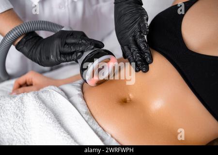 Chiudere il cosmetologo utilizzando il dispositivo a ultrasuoni durante l'esecuzione della procedura di sollevamento sulla pancia della donna. Foto Stock