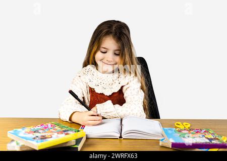 Un bambino felice è seduto a una scrivania e sorride mentre scrive su un notebook. Sta usando forniture per ufficio e un attrezzo per scrivere. Condividere il suo tempo libero Foto Stock