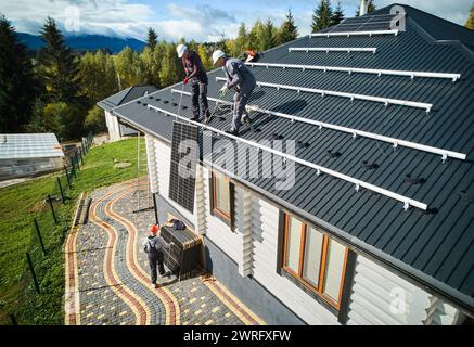 Lavoratori professionisti che sollevano il pannello solare su un tetto di casa. Due tecnici che trasportano un modulo solare fotovoltaico. Concetto di energia alternativa e rinnovabile. Foto Stock
