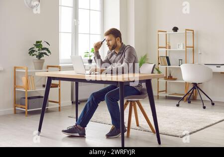 Uomo con barba concentrato che lavora a casa con un computer portatile Foto Stock