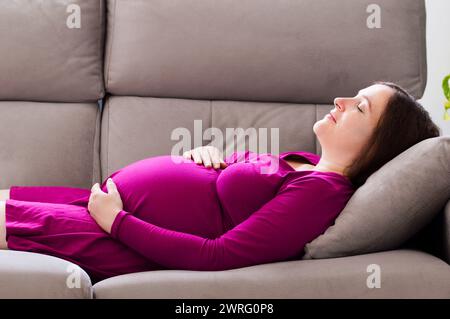 Ritratto di una donna incinta stanca che dorme su un divano nel soggiorno di casa Foto Stock