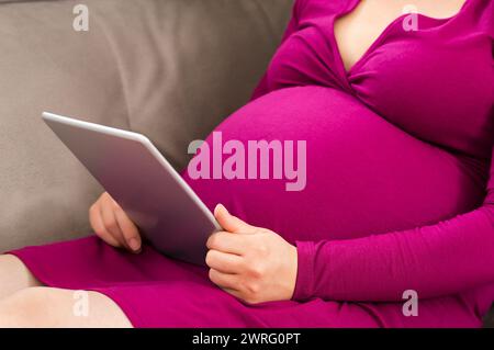 Primo piano di una donna incinta testando sul suo tabet a casa Foto Stock