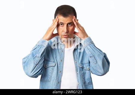 Studio girato di un giovane uomo con un'espressione facciale scomoda a causa di un mal di testa, mentre in piedi su uno sfondo grigio Foto Stock