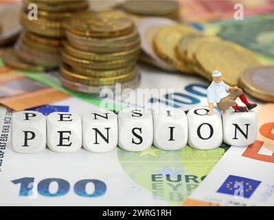 I cubi di legno formano la parola PENSIONE su fondo monetario in euro con banconote e monete Foto Stock