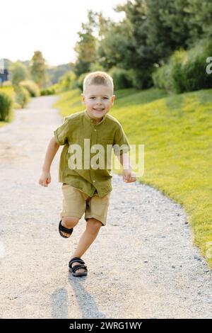 Un ragazzo corre energicamente lungo un sentiero sterrato circondato dal verde in una giornata di sole. Foto Stock