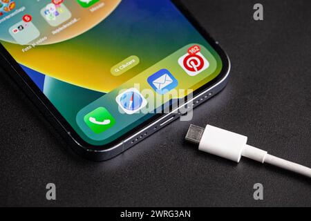L'immagine dell'iPhone con il caricabatterie tipo c accanto, che è il cambiamento dell'anno nella tecnologia telefonica, su sfondo nero.Hincesti Foto Stock