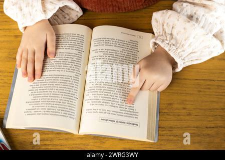 Una persona è seduta ad un tavolo di legno, la mano riposa su un libro. Sono coinvolti nella pubblicazione, facendo gesti con le dita mentre leggono Foto Stock