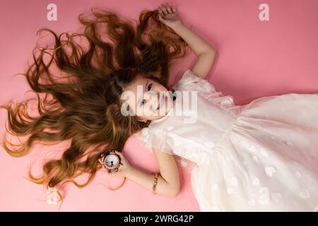 Una bambina molto bella e carina che sta sdraiata su uno sfondo rosa con i capelli sciolti e posati molto bene, capelli marroni e molto soffice e lucente Foto Stock