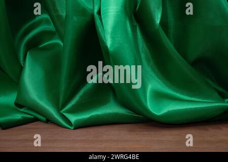 Pavimento in legno vuoto con eleganti tende in tessuto satinato verde ondulato, sfocate sullo sfondo, sfondo del posizionamento dei prodotti Foto Stock