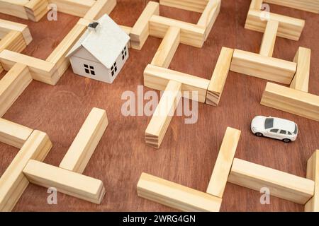 Auto in miniatura che trova la strada per una casa bianca in un labirinto di legno, metafora psicologica, messa a fuoco morbida in primo piano Foto Stock