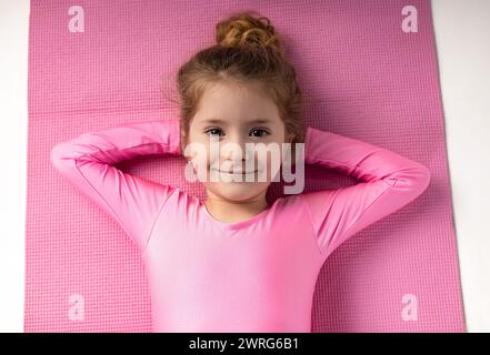 Ritratto di una piccola ginnasta con le mani sotto la testa sdraiate sul tappetino da yoga dopo gli esercizi. Foto di alta qualità Foto Stock